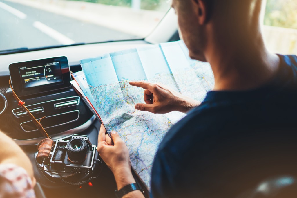 Hipster man looking and point finger on location navigation map in car.