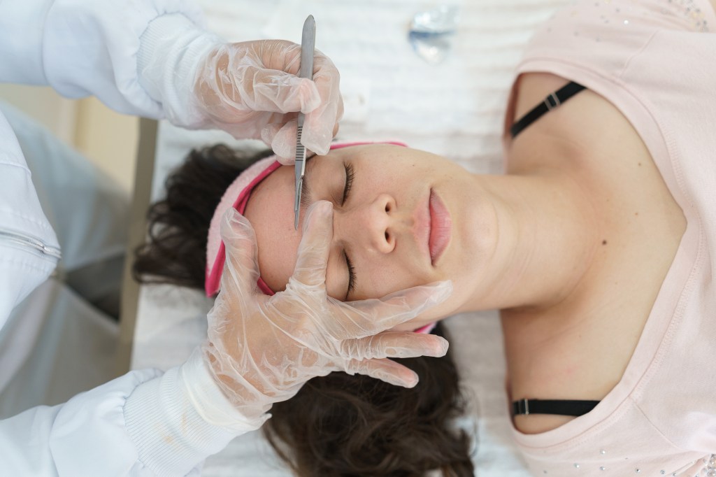 A beautician performing dermaplaning treatment on a woman.