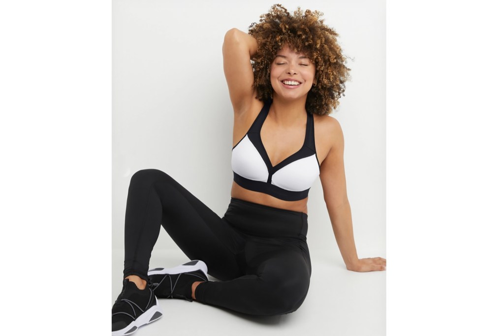 A woman sitting in black leggings and a white sports bra smiling 