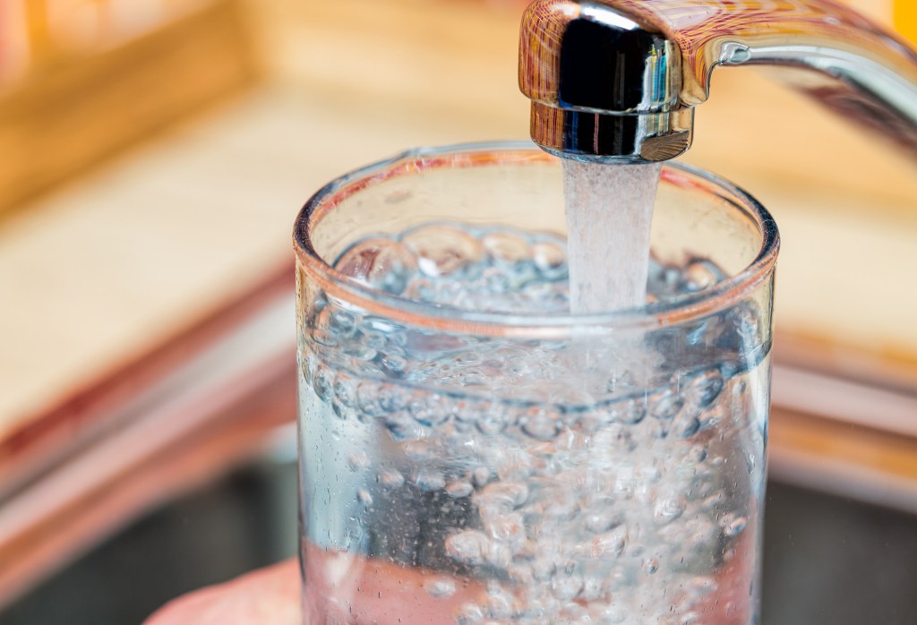 Man fills glass with fresh water from kitchen faucet.