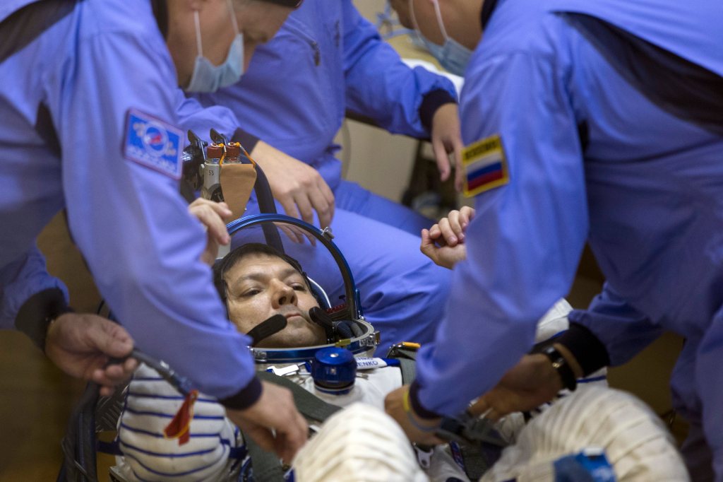 Russian cosmonaut Oleg Kononenko in a white space suit and others preparing for a space mission with Soyuz-FG booster rocket.