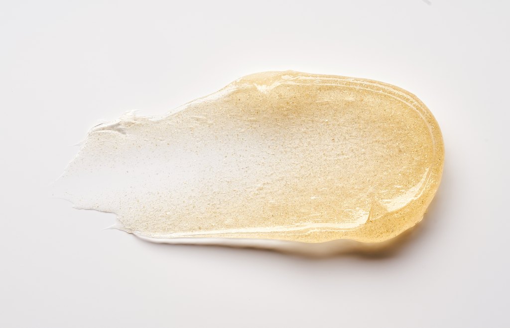 Transparent smear of golden cosmetic gel on white background.