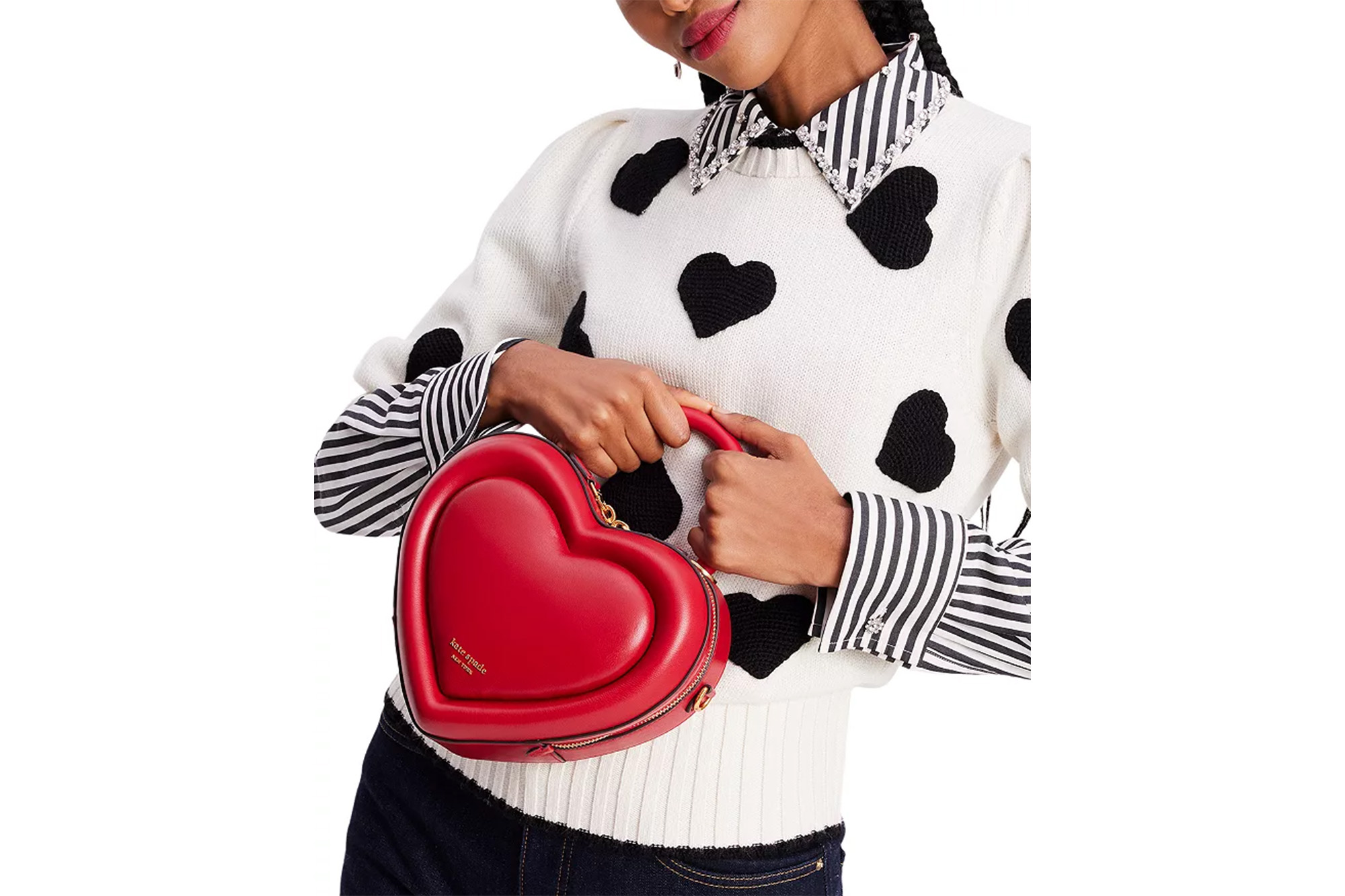 A model in a heart sweater holding a red purse