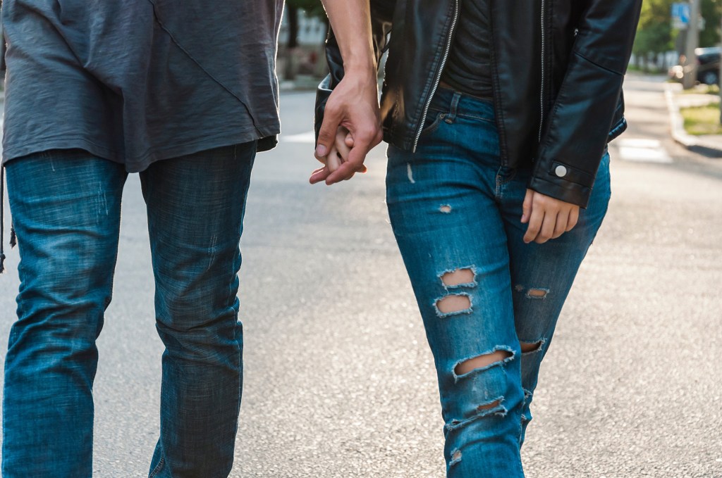 Man and woman's arms and legs while holding hands walking down the street in jeans and T-shirts.