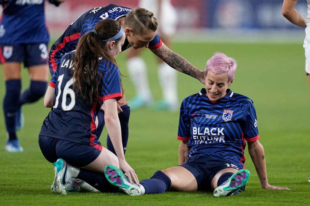 OL Reign forward Megan Rapinoe down on ground surrounded by teammates Rose Lavelle (16) and Jess Fishlock during NWSL Championship soccer game.