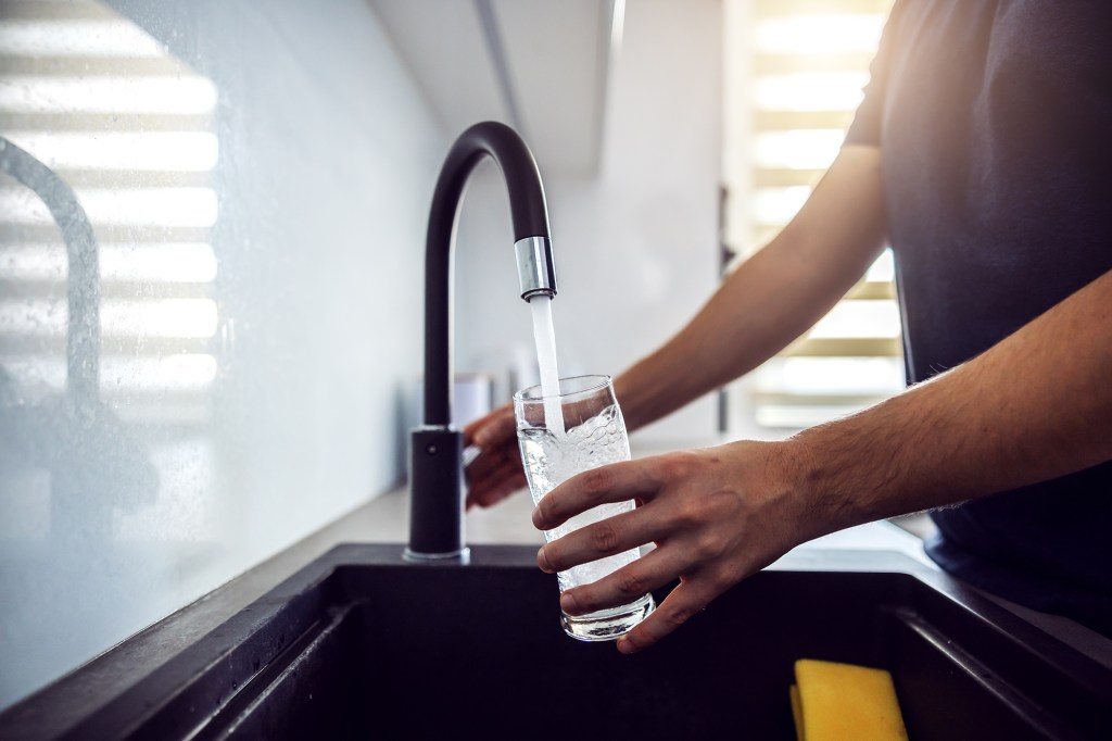 Young man pouring fresh water from kitchen sink.