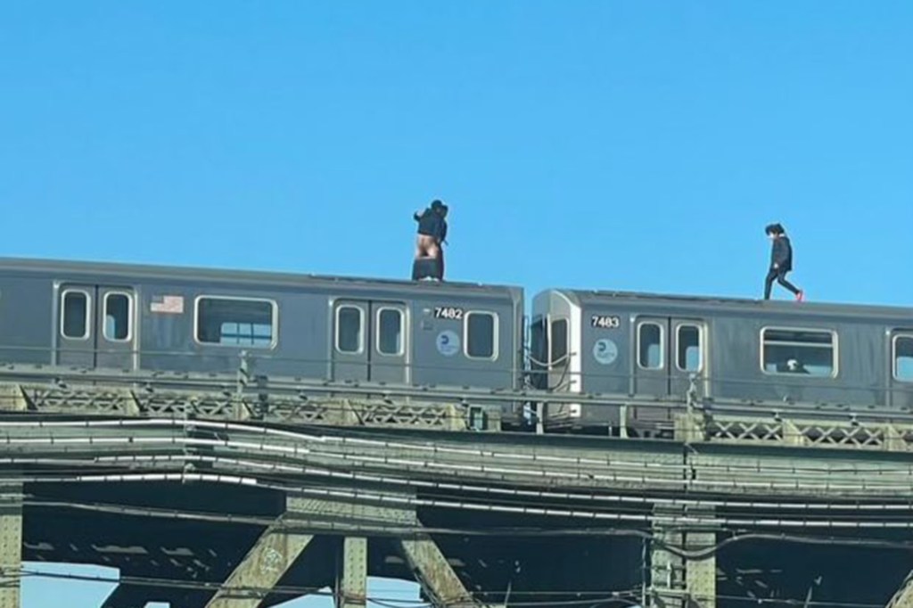 Man with exposed buttocks stands atop train car as another man walks toward him 