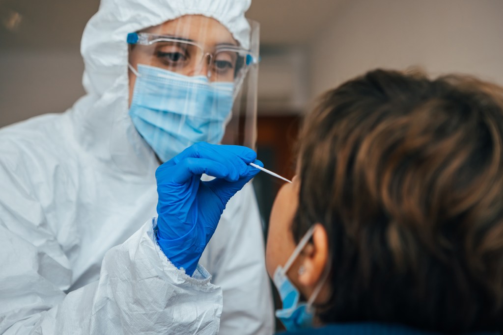 Close up of female health Professional in PPE introducing a nasal swab to a senior female patient at her house