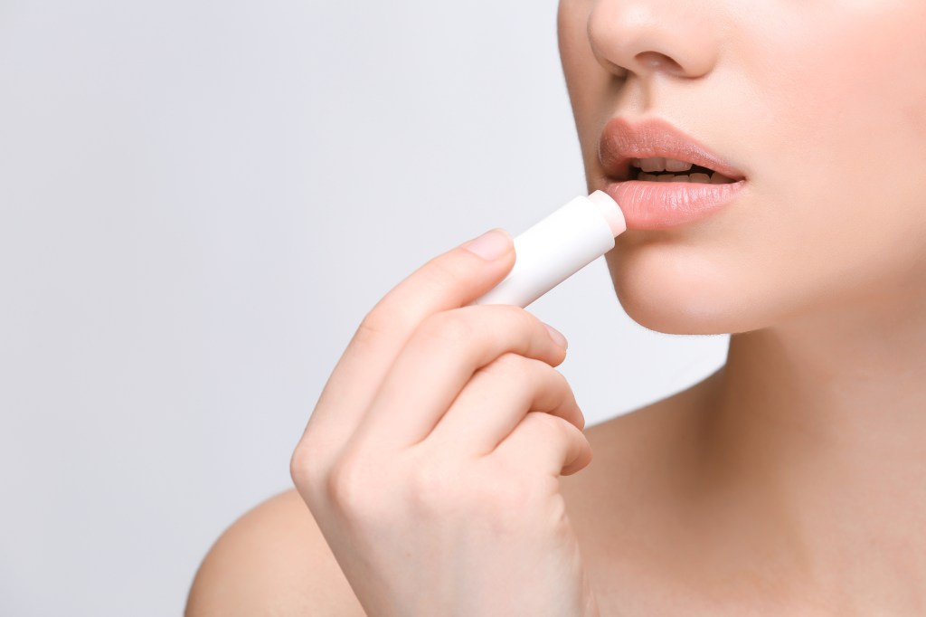 Woman applying hygienic lip balm on a light background