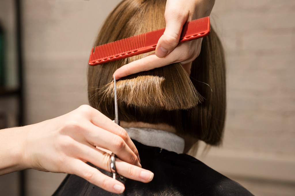 Back view of a preteen girl in a salon chair, hairdresser checking her new bob haircut