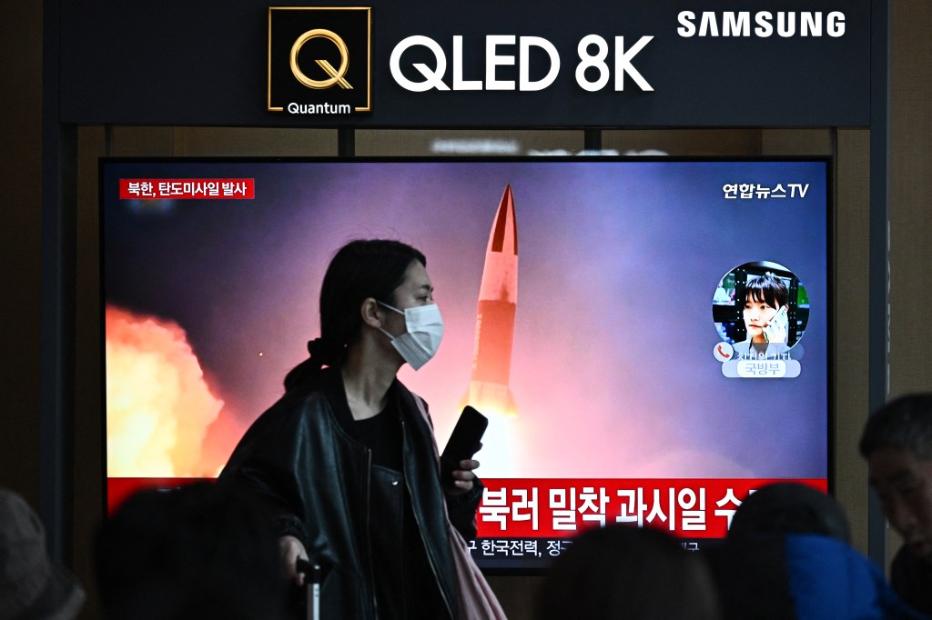 A woman walks past a television showing a news broadcast with file footage of a North Korean missile test, at a railway station in Seou