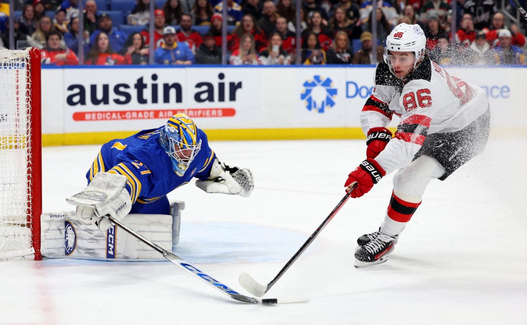 Sabres goaltender Devon Levi (27) knocks the puck off the stick of New Jersey Devils center Jack Hughes