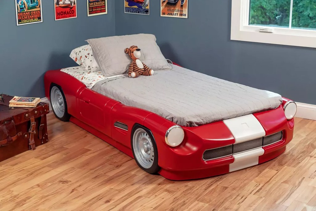 A red car-shaped bed with a stuffed animal on top