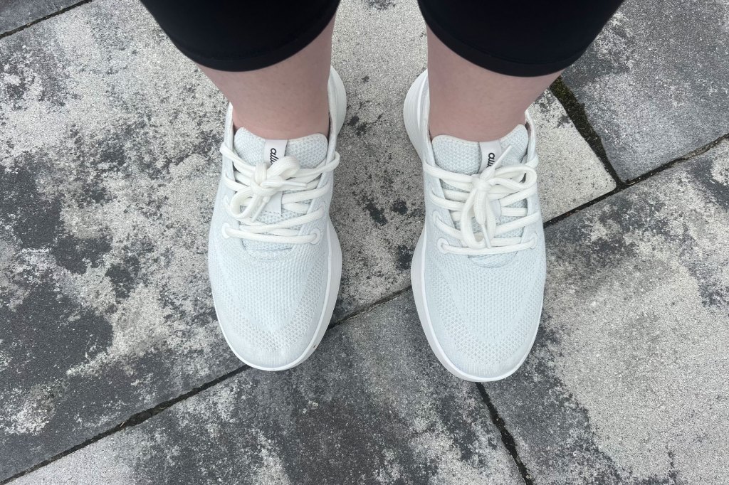 A person's feet wearing white Allbirds shoes