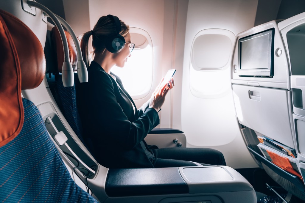 Caucasian female airplane passenger reading received email via mobile phone during trip connected to wireless internet on board