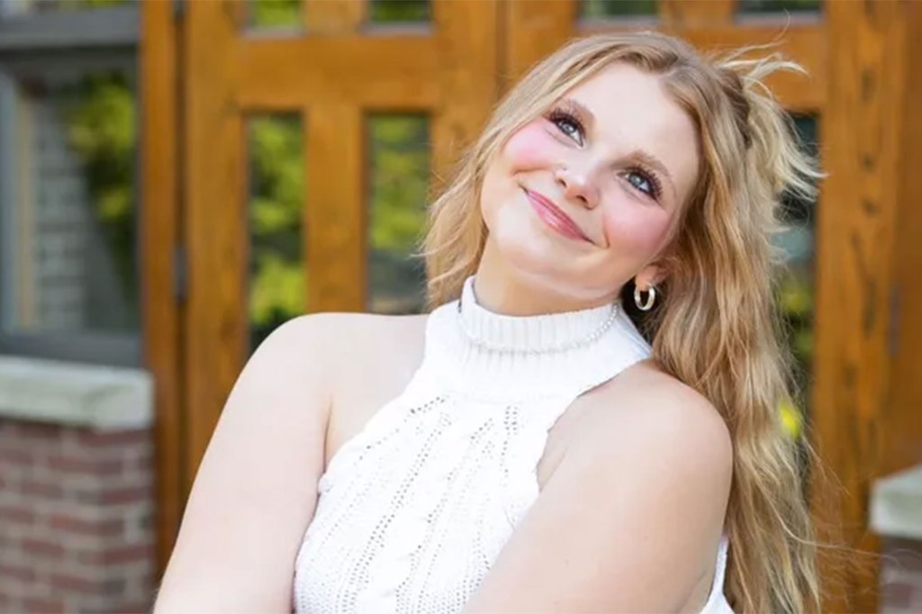 A smiling woman in a white tank top looks up.