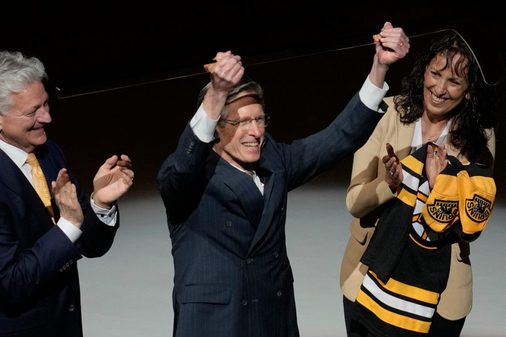 Boston Bruins television play-by-play announcer Jack Edwards, center, holds up a golden stick in honor of his announced retirement, before the Bruins' NHL hockey game against the Ottawa Senators, Tuesday, April 16, 2024, in Boston. 