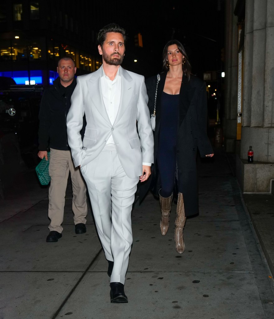 Scott Disick in a grey suit walking with model Bella Banos in a black dress towards Nobu in New York City