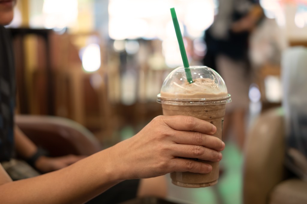 Woman holding a slimmed down plastic glass of iced coffee with milk and a straw