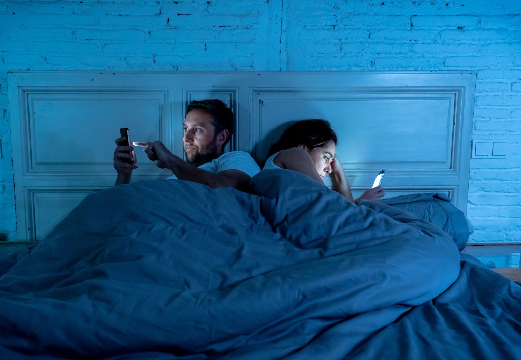 A couple lying in bed late at night, absorbed in their mobile phones, showing signs of technology addiction and relationship issues