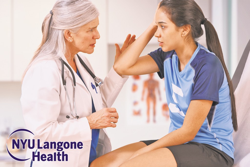 Young athlete sitting with hand on head talking to a doctor