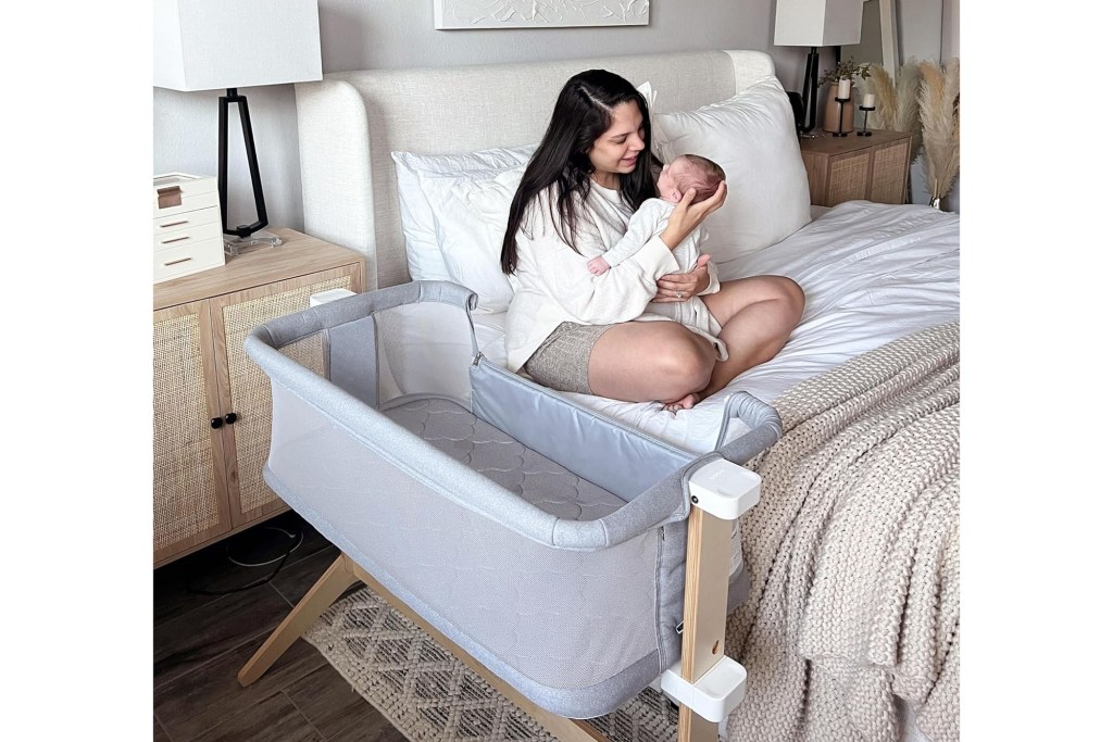 A woman holding a baby near a bassinet