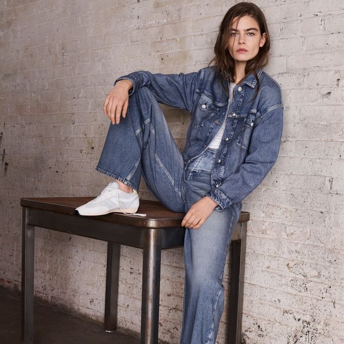 A woman sitting on a table wearing the viral Rag & Bone Miramar sweatpant-jeans with a realistic denim print and slouchy fit.