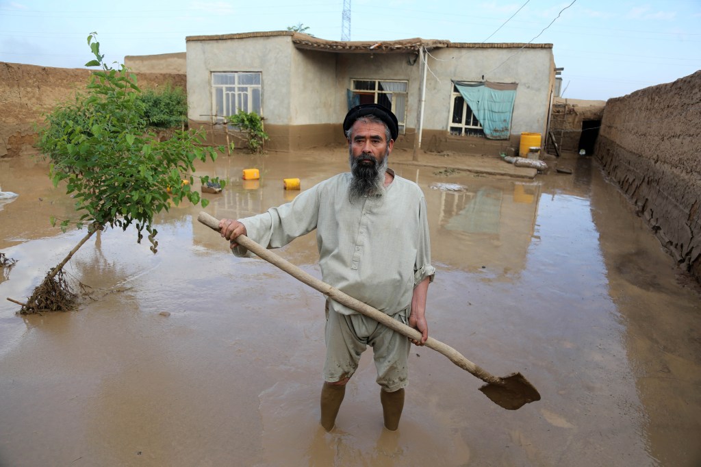 A man holding a shovel surveying his damaged house after flash floods in Shahrak Muhajireen village, Baghlan, Afghanistan.