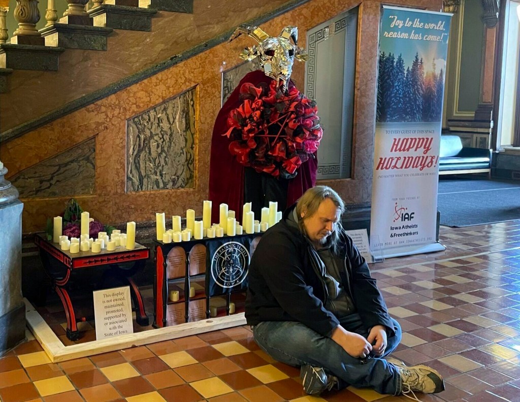 Man praying in front of a Satanic Temple Iowa display at Iowa State Capitol, which was later vandalized