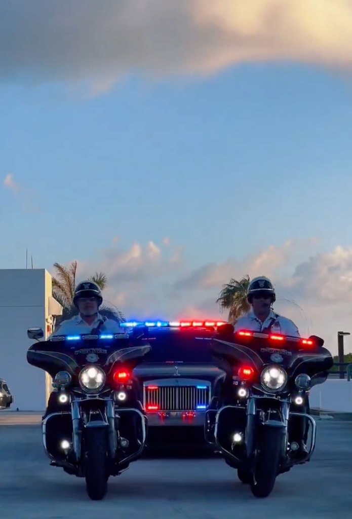 Two police officers on motorcycles with flashing lights, part of the Miami Beach Police Department recruitment team