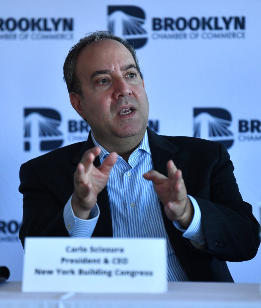 Carlo Scissura seated at a table with a white sign with black letters with his name in the foreground