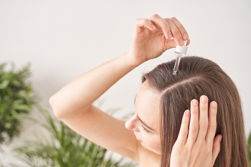 Young woman applying Argan oil hair treatment with a dropper in her bathroom routine