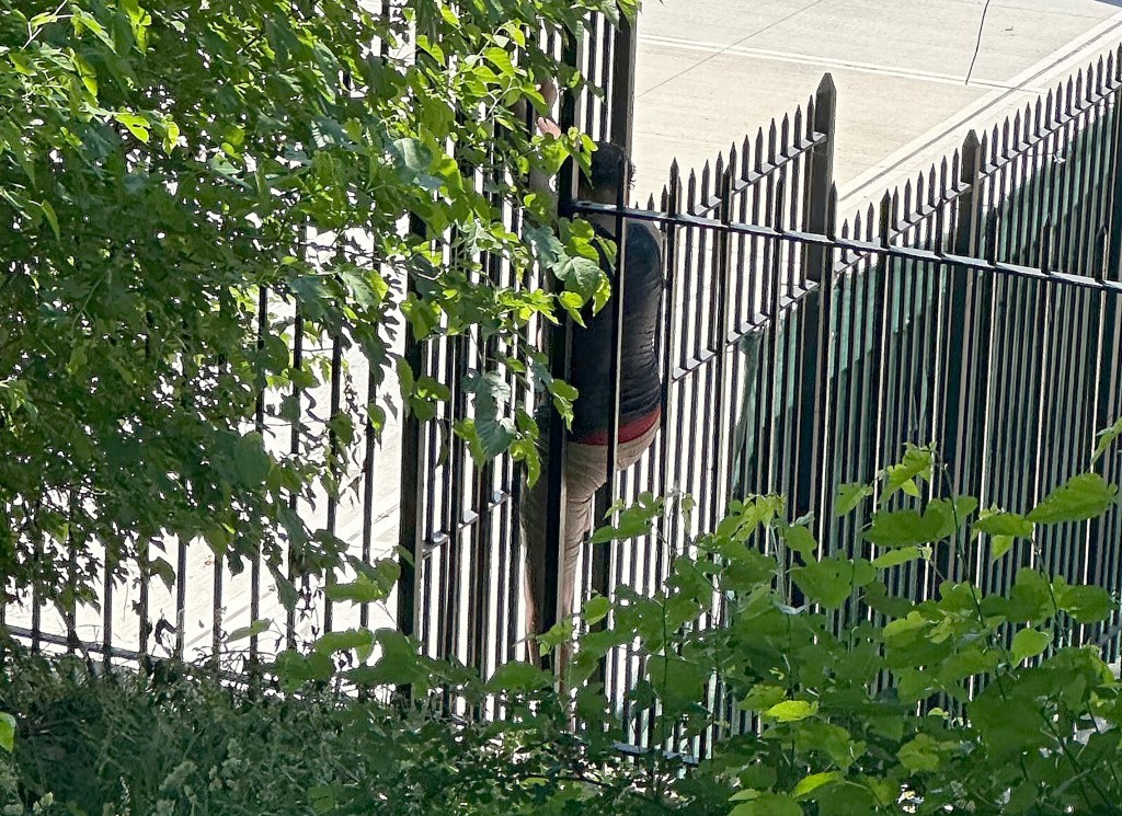 Man climbing over a black metal fence to enter the closed Astoria Pool at Astoria Park in Queens, NY for a swim