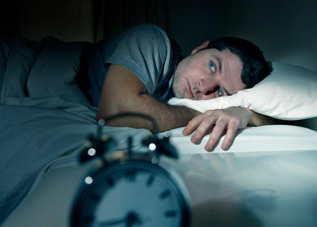 Young man lying in bed with open eyes, suffering from insomnia and sleep disorder, thinking about his problem.