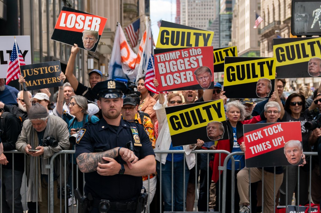 Anti-trump protestors gathered  behind a metal barricade outside Trump Tower following Thursday's verdict with large yellow and black signs reading "GUILTY" and a police officer standing in front of the barricade looking at the camera