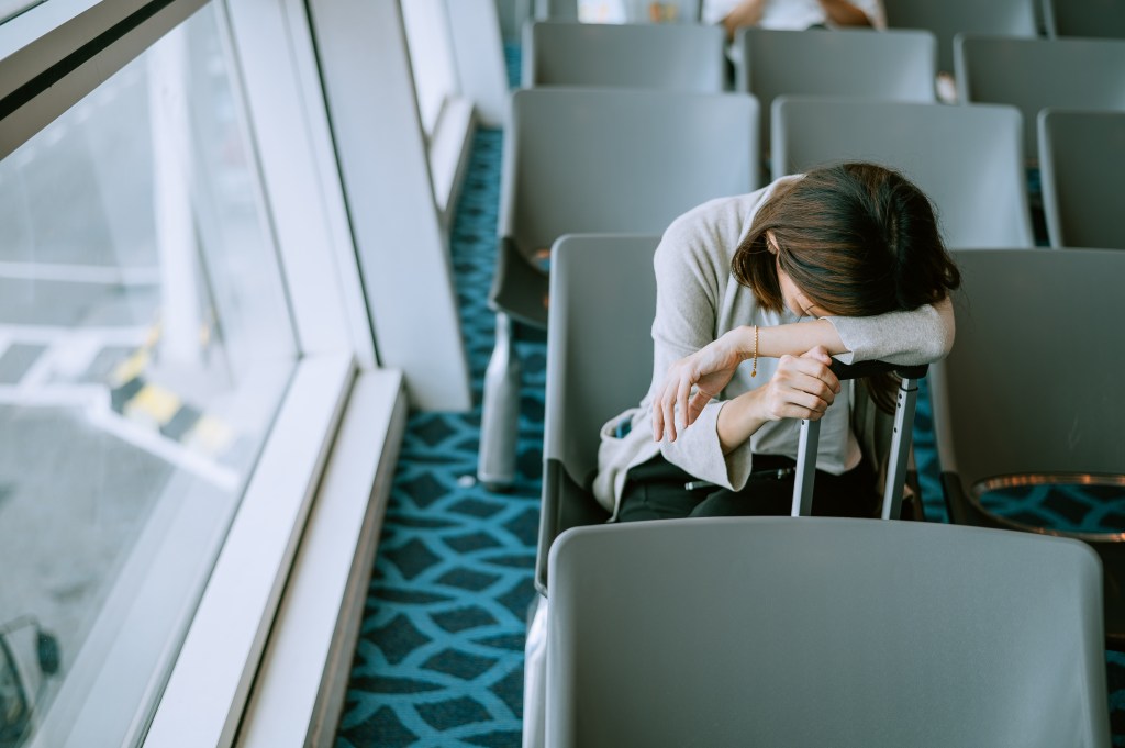 Young woman sleeping in a chair at an airport waiting area with a commercial airplane in the background