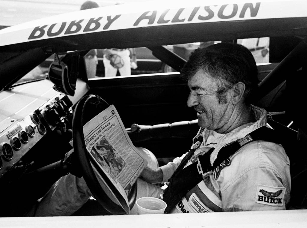 checks out the newspaper during qualifying trials for the Nashville Pepsi 420 NASCAR Grand National race at Nashville International Raceway on July 13, 1984.