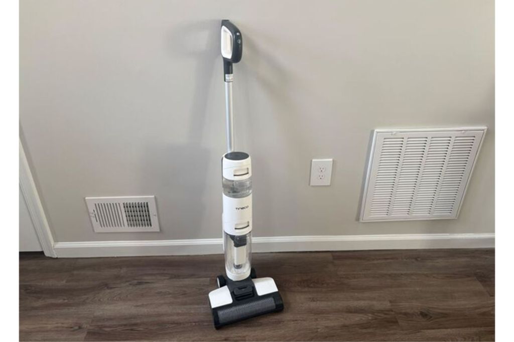 A white upright cordless vacuum against a wall in a hallway.