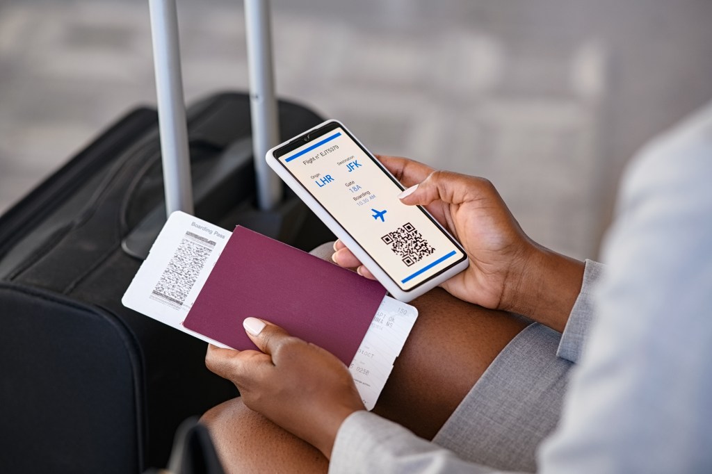 Close up hand of black businesswoman checking flight eticket on phone while holding passport and boarding pass