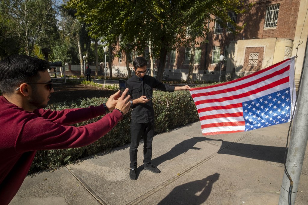 An Iranian man holding an upside-down US flag while being photographed by his friend at the former US embassy in Tehran, Iran.