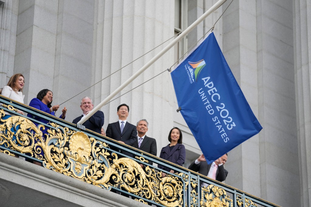 San Francisco Mayor London Breed, second from left, raises the APEC Summit flag over a balcony at City Hall