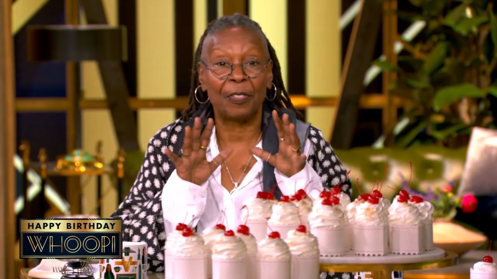 Whoopi Goldberg sitting at a table with cupcakes, discussing a dispute with a bakery over her political views