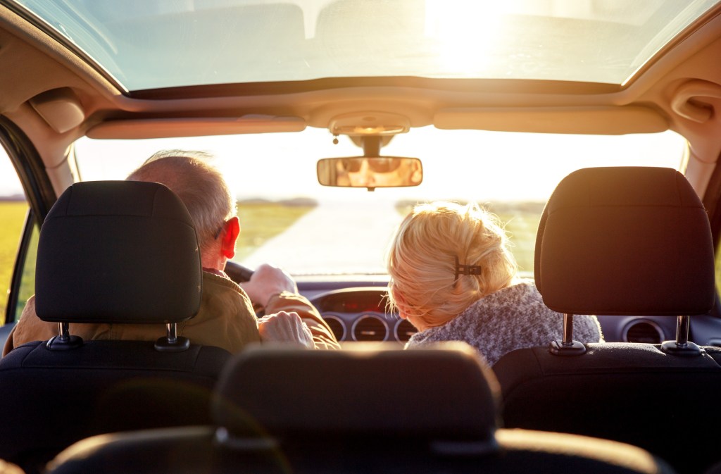 Rear view of smiling elderly couple driving car.