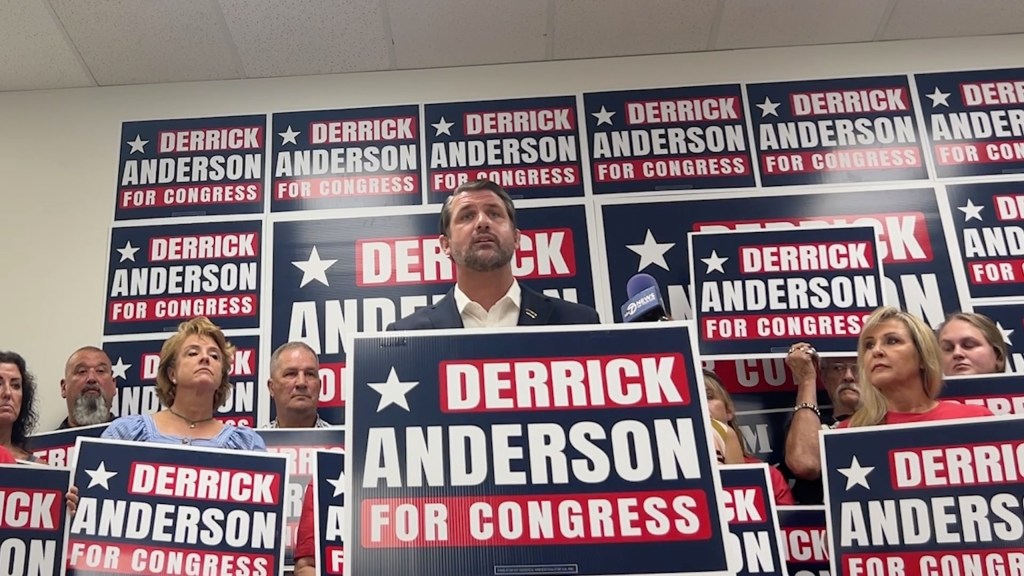 Derrick Anderson, GOP candidate, standing behind a podium with signs.