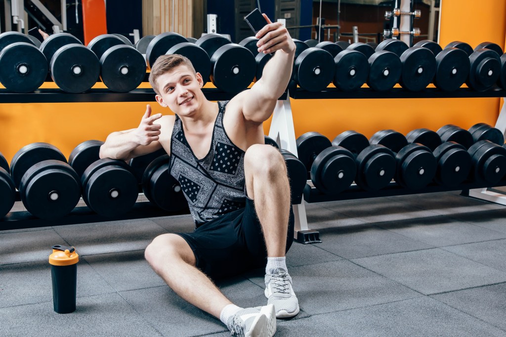 A man takes. a selfie in front of a rack of weights at the gym.