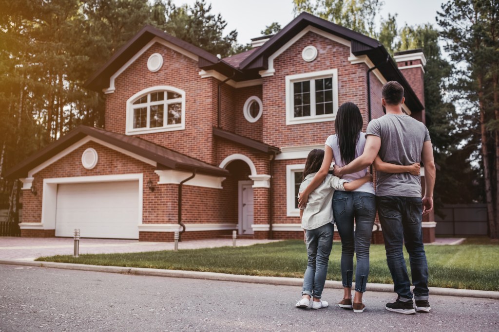 Back view of a happy family hugging in front of their modern house