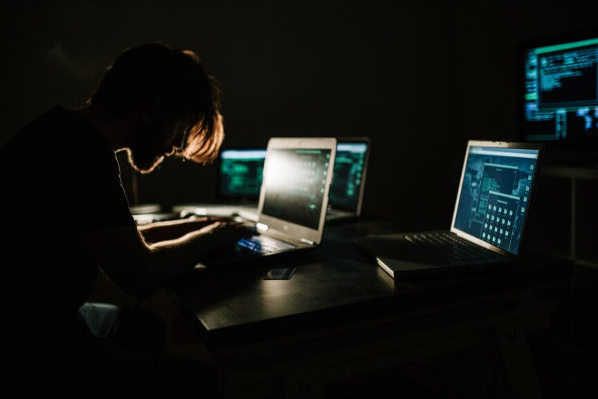 cream_ph. Getty Images. Young hacker working in the dark room and using laptops to steal private information