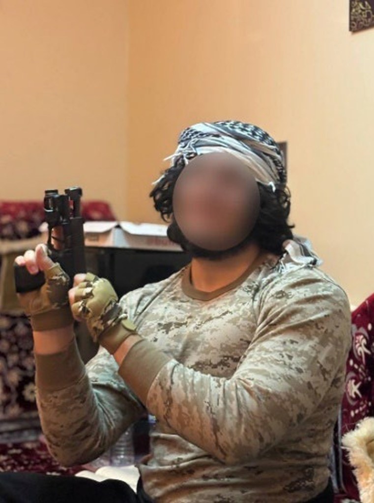 A person wearing a tactical shirt and headscarf holds a pistol, with their face blurred out.