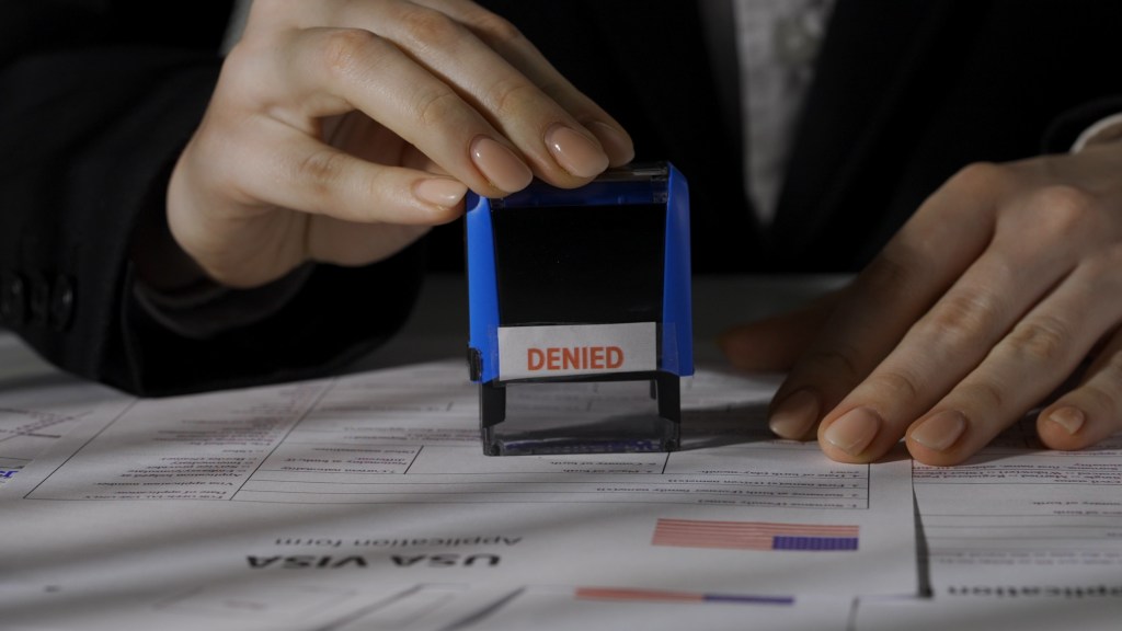 Female worker's hands stamping "DENIED" on a USA visa application document.