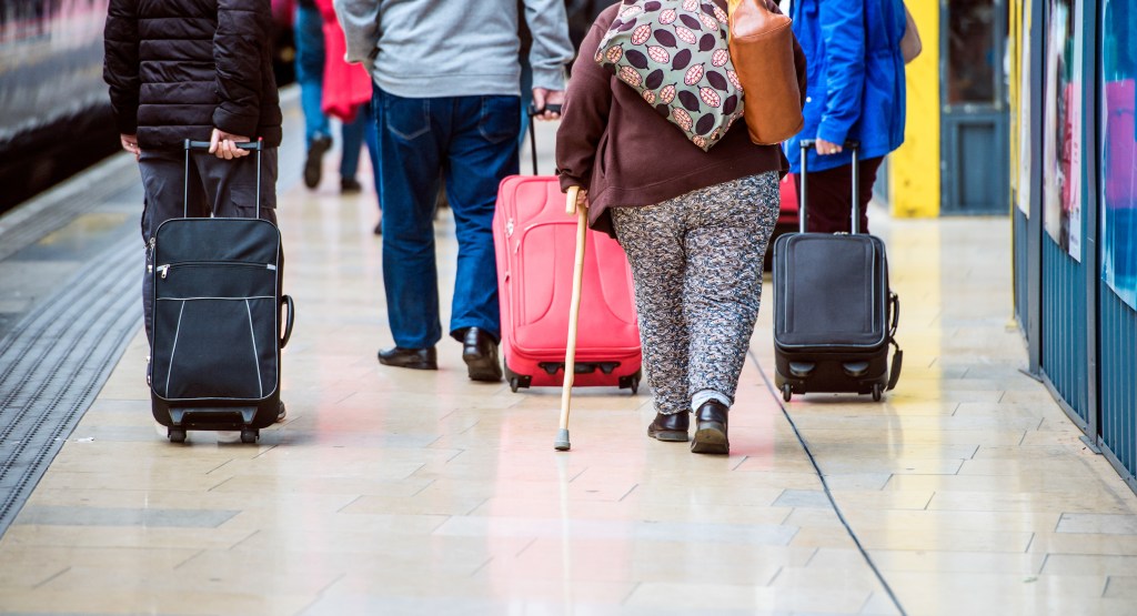 Travellers walking with luggage through a train station in London.